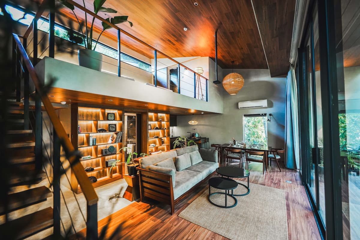 Een modern interieur met een houten trap, een bank, een eettafel en een groot raam.