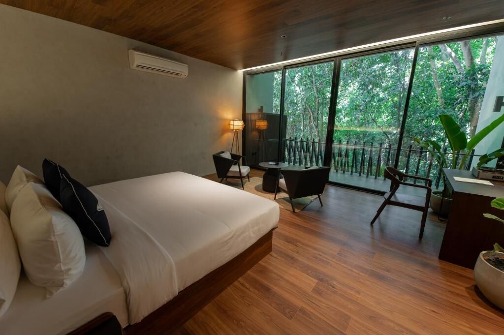 Quarto de hotel moderno com uma cama grande, uma escrivaninha e uma varanda com vista para a floresta.
