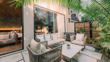 A modern outdoor seating area with a sofa, chairs, and a table, surrounded by greenery and a large window.