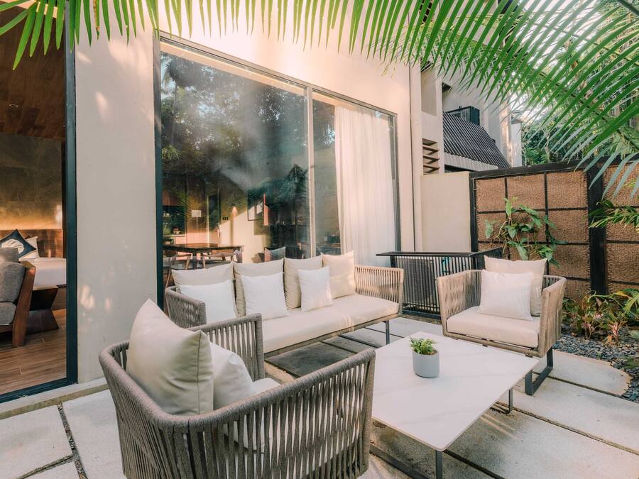 A modern outdoor seating area with a sofa, chairs, and a table, surrounded by greenery and a large window.
