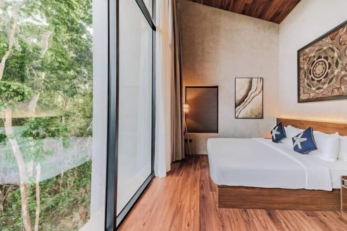 Een moderne slaapkamer met een groot raam, een bed met wit beddengoed en een houten plafond.