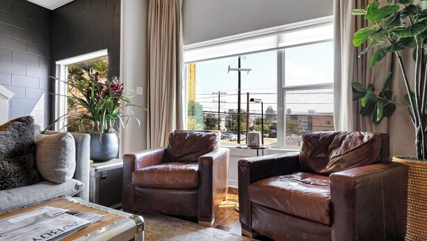 Ein modernes Wohnzimmer mit Ledersesseln, einer Couch, einem Couchtisch und einem großen Fenster mit Blick auf die Stadt.