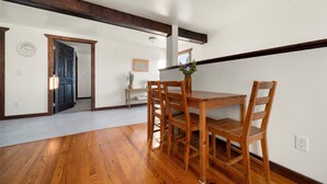 Un coin repas avec une table et des chaises en bois, une petite console sur laquelle est posé un vase de fleurs, et une horloge au mur.