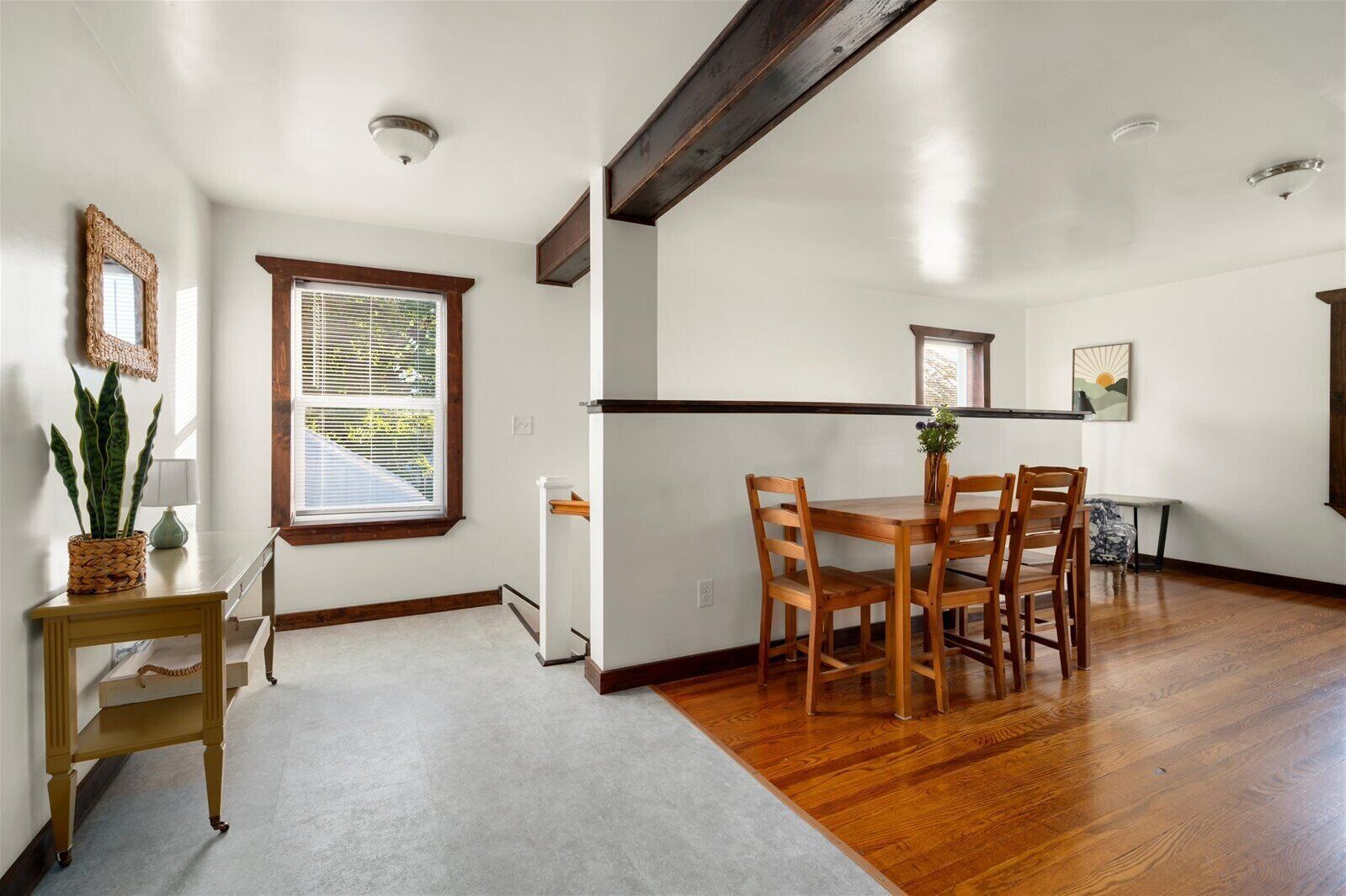 Un coin repas avec une table et des chaises en bois, une fenêtre avec des stores, un radiateur et une plante posée sur une petite table.