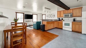 Une cuisine moderne avec des meubles en bois, un coin repas avec une table et des chaises, et un téléviseur fixé au mur.