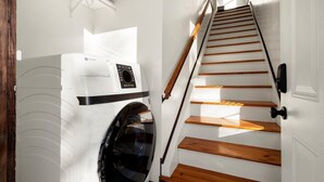 Un espace buanderie équipé d’un lave-linge et d’un sèche-linge, d’un escalier en bois et d’une porte blanche.