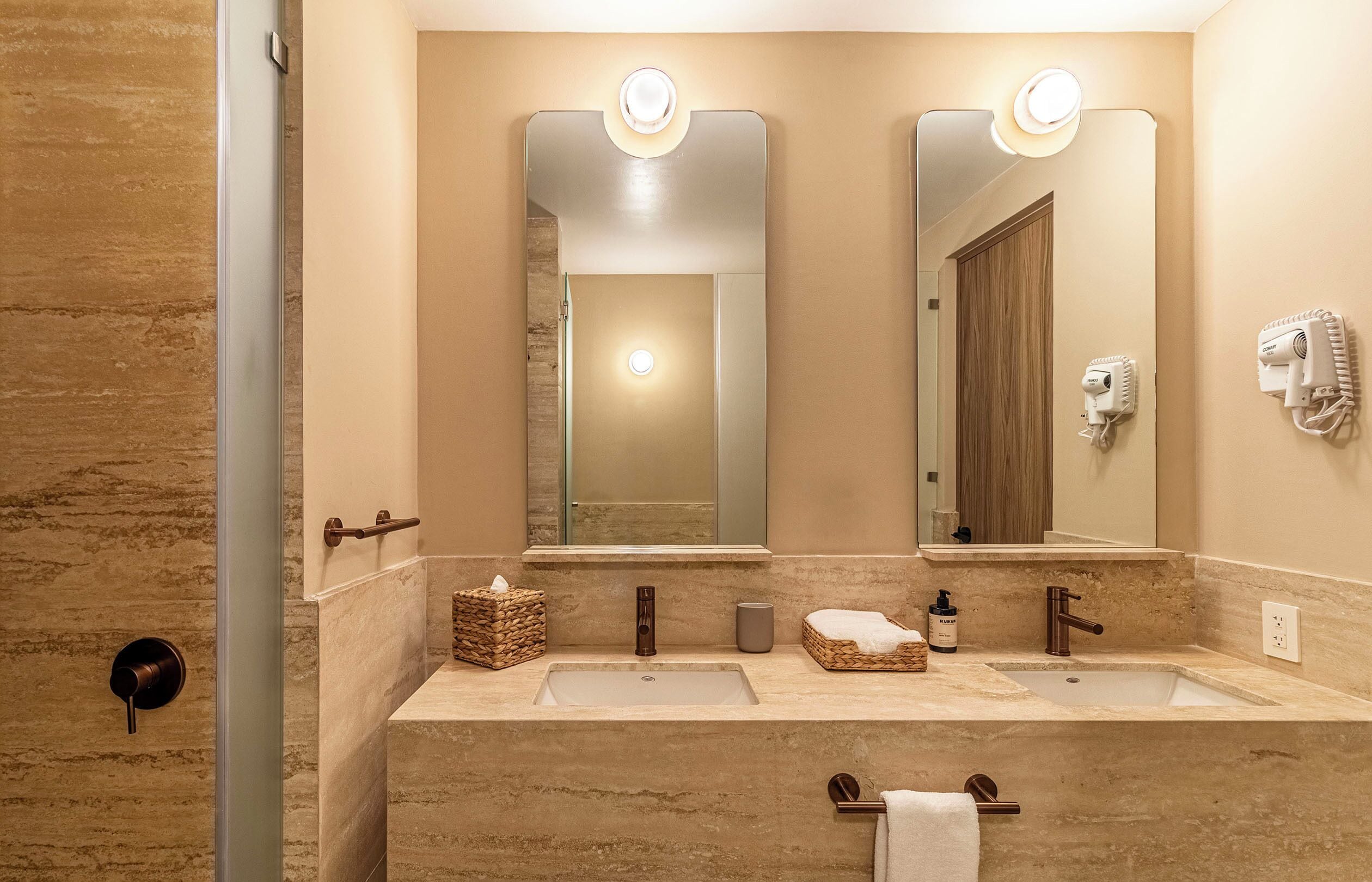 A bathroom with two sinks, a mirror, a towel rack, a hairdryer, and a bottle of hand soap.