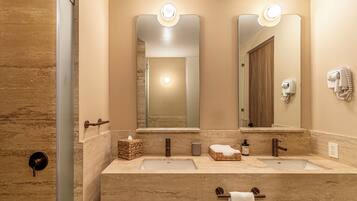 Une salle de bain avec deux lavabos, un miroir, un porte-serviettes, un sèche-cheveux et un flacon de savon pour les mains.