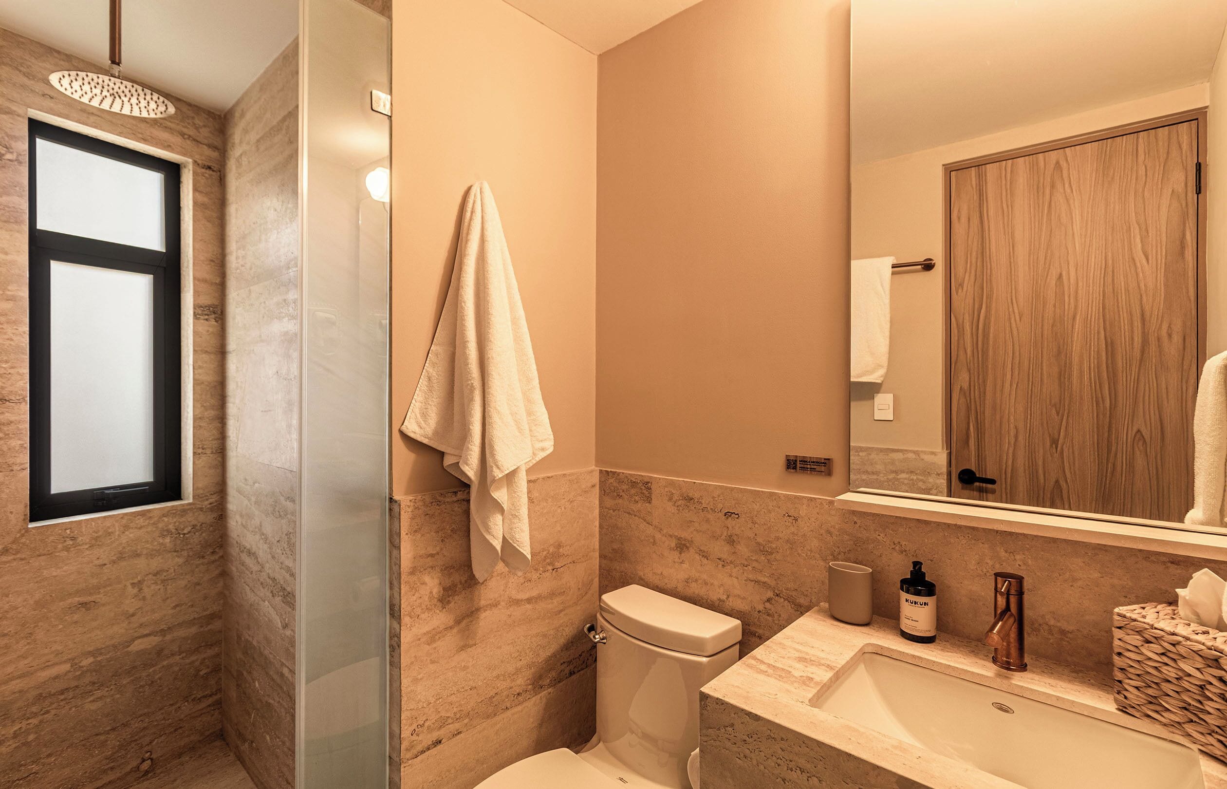 Une salle de bain moderne avec une douche à parois de verre, des toilettes, un lavabo et un miroir qui reflète une porte en bois.