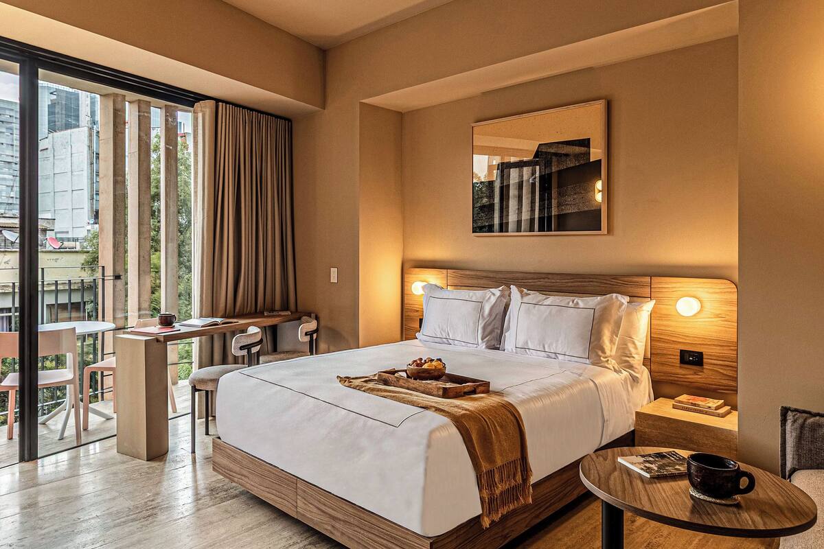 A hotel room with a large bed, bedside tables, a desk, and a view of the city.