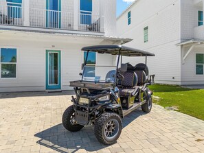 A golf cart parked in front of a white building with a blue door and windows.