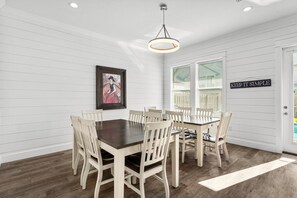 A dining room with a dark wooden table and white chairs, white paneled walls, a framed picture, and a sign that says "KEEP IT SIMPLE".