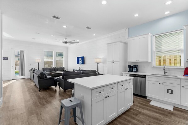 A modern kitchen with white cabinetry, a central island, and a dining area with a gray sofa.