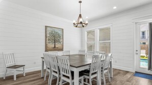 A dining area with a round table and white chairs, white walls, and a chandelier.