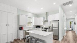A modern kitchen with white cabinetry, a large island with stools, stainless steel appliances, and a bright, well-lit space.