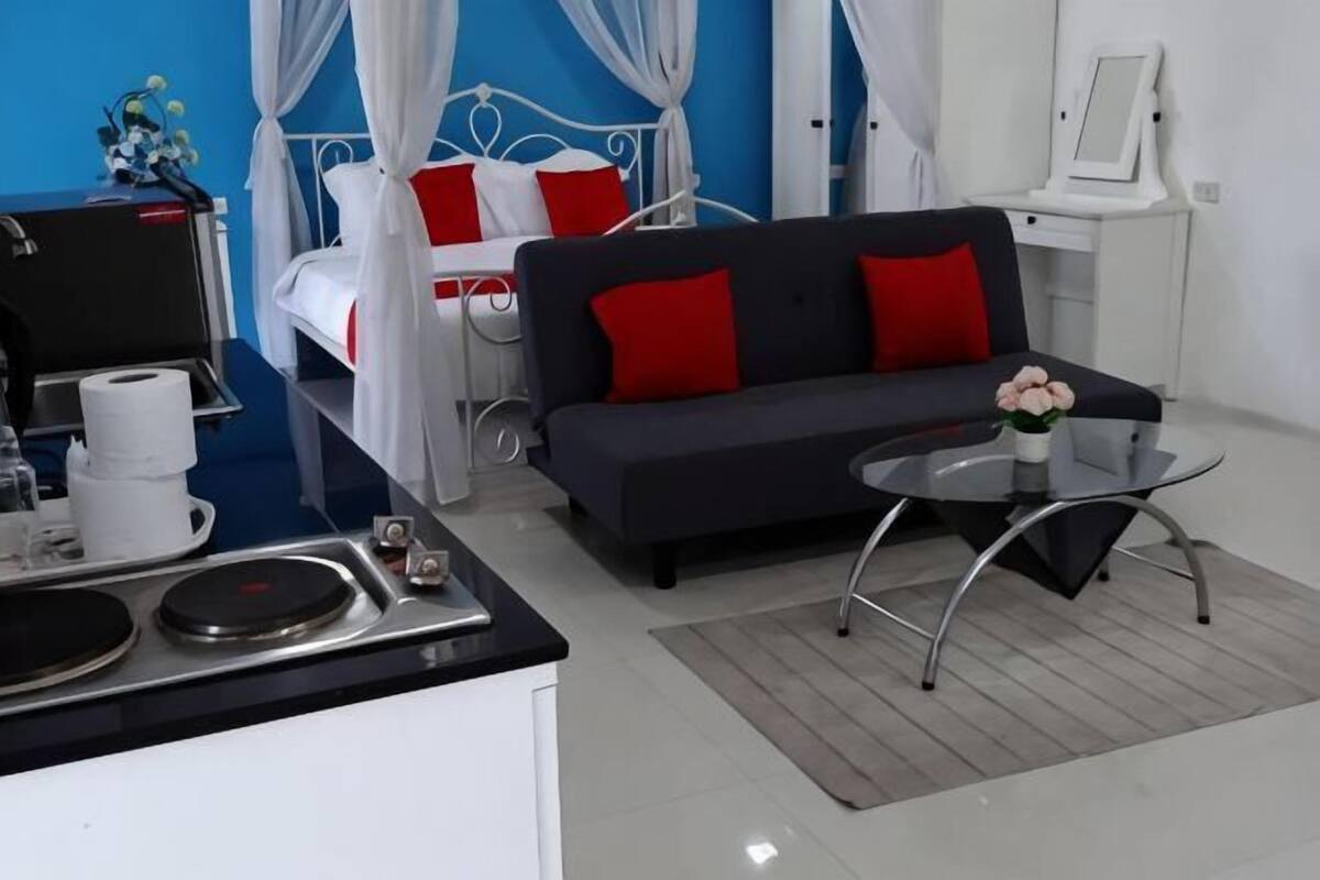 A modern hotel room with a bed, a sofa, a small table, a mirror, and a kitchenette.