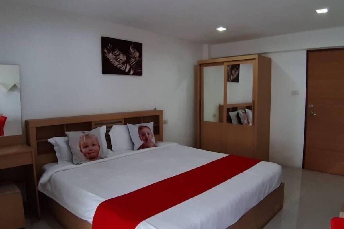 A bedroom with a bed, a wooden wardrobe, a mirror, and a wall-mounted artwork.