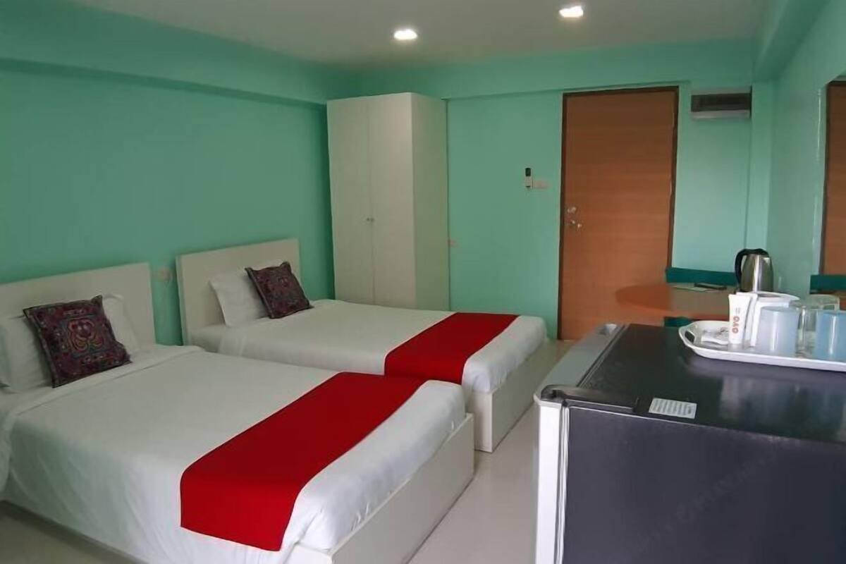 A room with two beds, a wardrobe, a desk with a kettle, and a door.