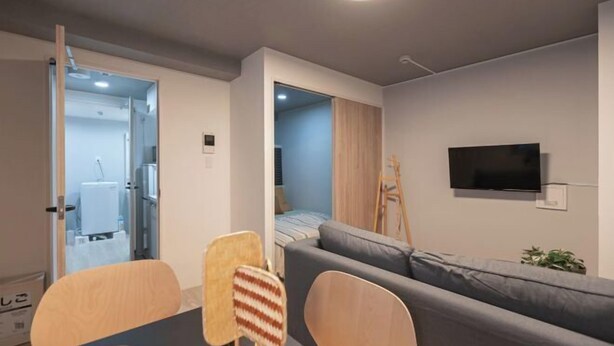 A modern living room with a sofa, chairs, a TV, and a doorway leading to another room. - Mi-HOTEL OTSUKA (Tokyo)