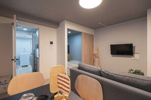 A modern living room with a sofa, chairs, a TV, and a doorway leading to another room. - Mi-HOTEL OTSUKA (Tokyo)
