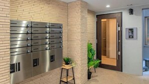 A modern hotel lobby with a brick wall, a row of metallic lockers, a small wooden table with a plant, and a door leading to the rooms. - Mi-HOTEL OTSUKA (Tokyo)