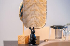 Ein gewebter Korb, eine schwarze Hasenfigur und eine klare Glas-Tasse auf einer Holztischplatte.