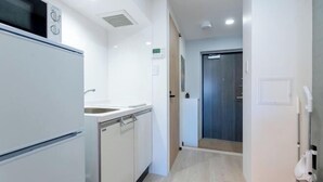 A modern kitchen with white appliances, a sink, and a wooden door leading to another room. - Mi-HOTEL OTSUKA (Tokyo)