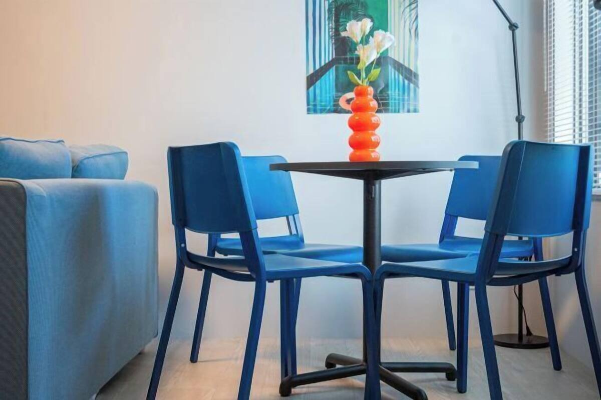 A room with a blue sofa, two blue chairs, a small black table, and a vase with flowers.