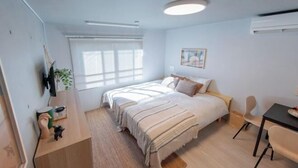 A modern bedroom with a bed, bedside table, chair, and a window with blinds. - Mi-HOTEL OTSUKA (Tokyo)