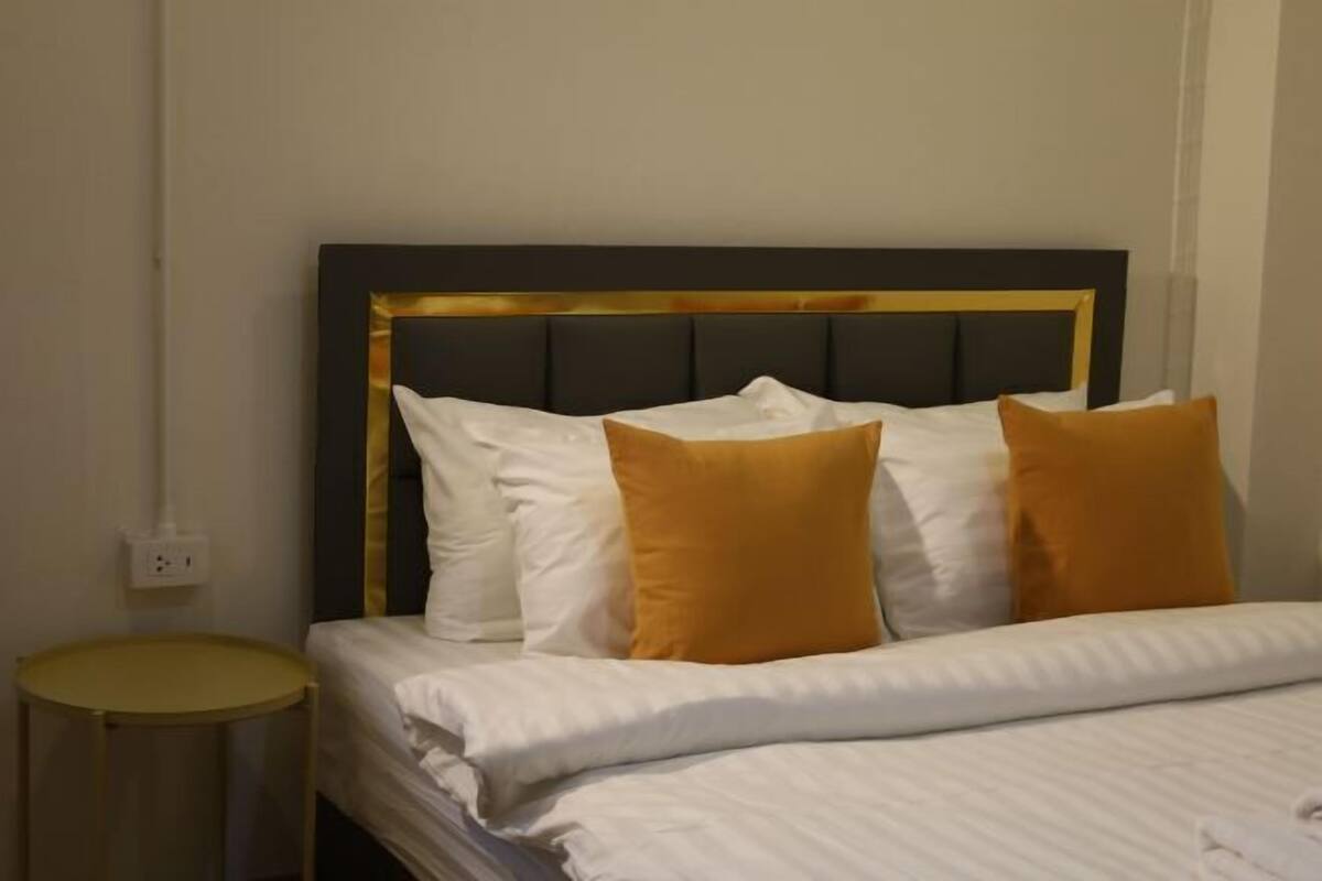 A bed with a dark headboard, white bedding, and two orange pillows.
