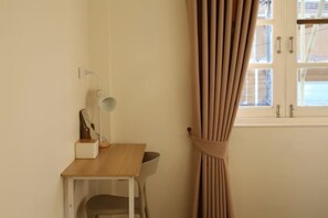 A room with a wooden desk, a chair, a mirror, and a window with curtains.
