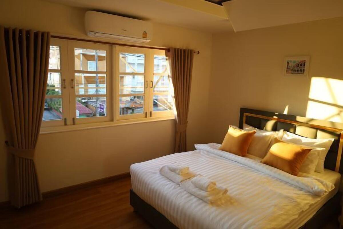A hotel room with a bed, curtains, an air conditioning unit, and a window.
