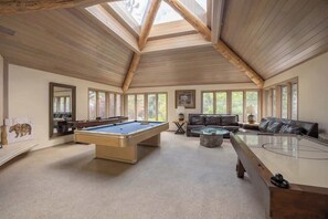 Un'ampia stanza con tavolo da biliardo, tavolo da snooker, divano e grandi finestre.