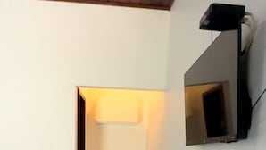 A small, narrow room with a bed, a white refrigerator, and a mounted television. - Salt Beach Guest House Atalaia (Salinópolis)