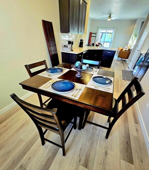 A dining area with a wooden table set for four, surrounded by chairs.