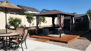 Un patio con mesa y sillas, una pérgola y una zona de estar cubierta.