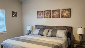 Un dormitorio con estructura de cama de madera, un ventilador de techo y cuatro adornos en la pared.