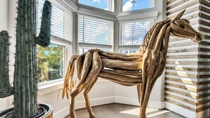 A room with a large wooden horse sculpture, a cactus, and a window with blinds.