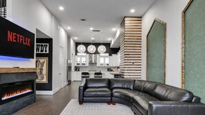 A modern living room with a fireplace, a leather sofa, and a kitchen in the background.
