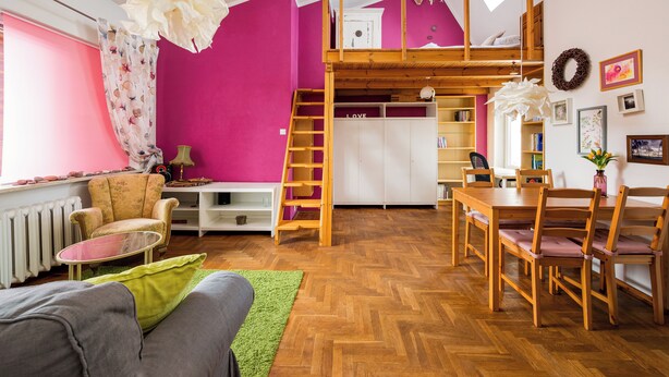 Una habitación con cama elevada, una mesa de comedor con sillas, un sofá, una mesita y un radiador.