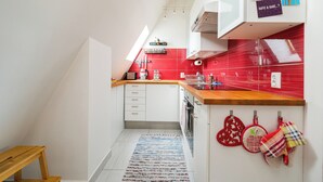 Una cocina moderna con armarios blancos, un salpicadero rojo y encimera de madera. Hay un taburete de madera pequeño y una alfombra azul y blanca a rayas en el suelo.