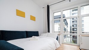 Une chambre moderne avec un grand lit, une vue sur un balcon et deux œuvres d’art jaunes accrochées au mur.