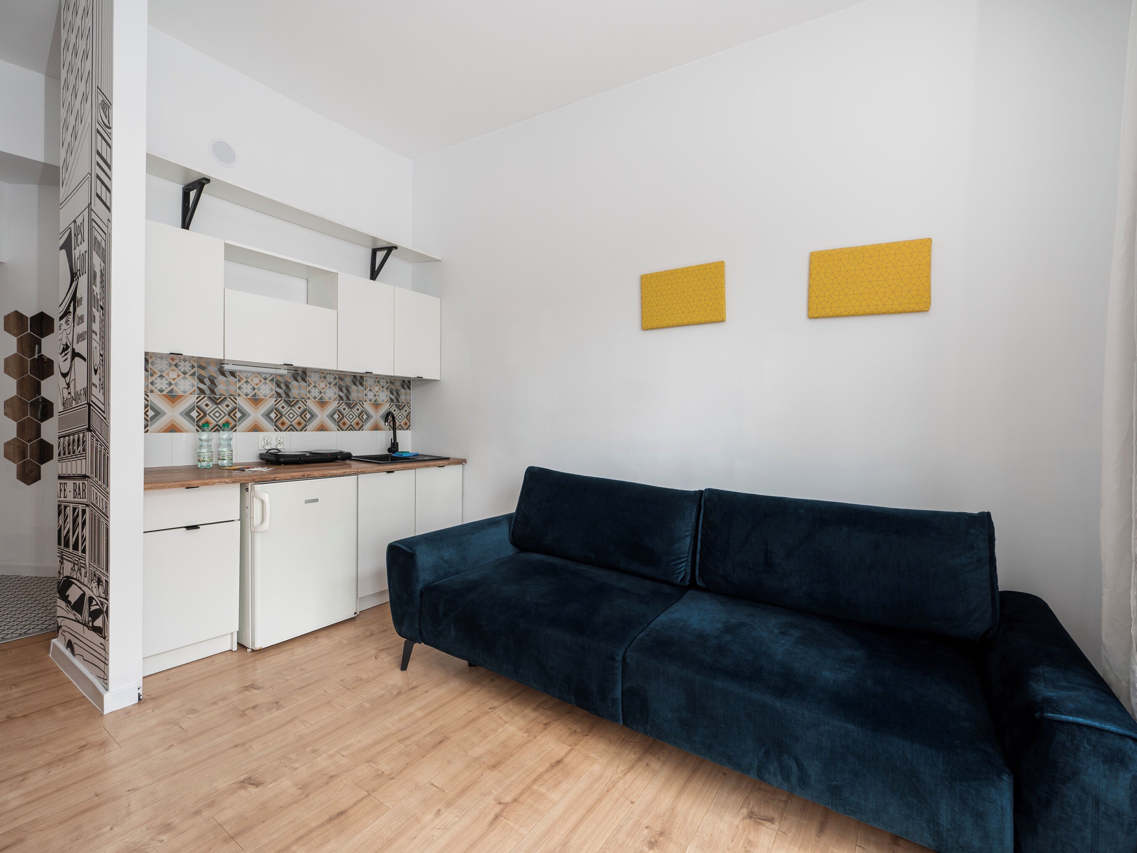 Una cocina moderna con armarios blancos, encimera de madera y un sofá azul en una sala de estar.