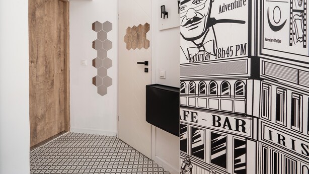 Un couloir avec une porte en bois, des carreaux hexagonaux recouvrant les murs, un téléviseur noir fixé au mur et un sol carrelé.