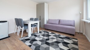 Un espace de vie compact comprenant une table blanche, deux chaises grises, un canapé violet et un tapis à motifs.