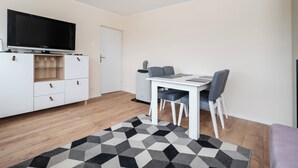 Un salon moderne doté d’un téléviseur à écran plat, d’un meuble blanc avec des tiroirs, d’une table à manger avec des chaises et d’un tapis à motifs.