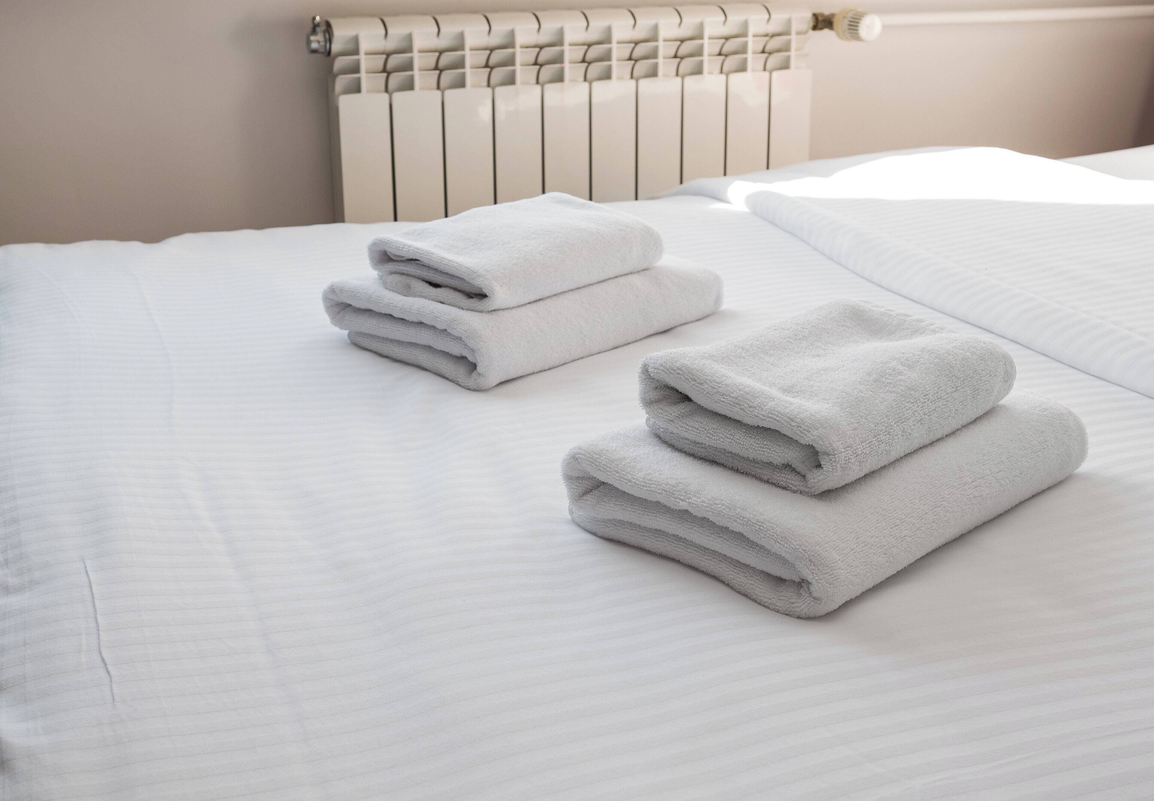 A neatly made bed with white linens and a radiator behind it.