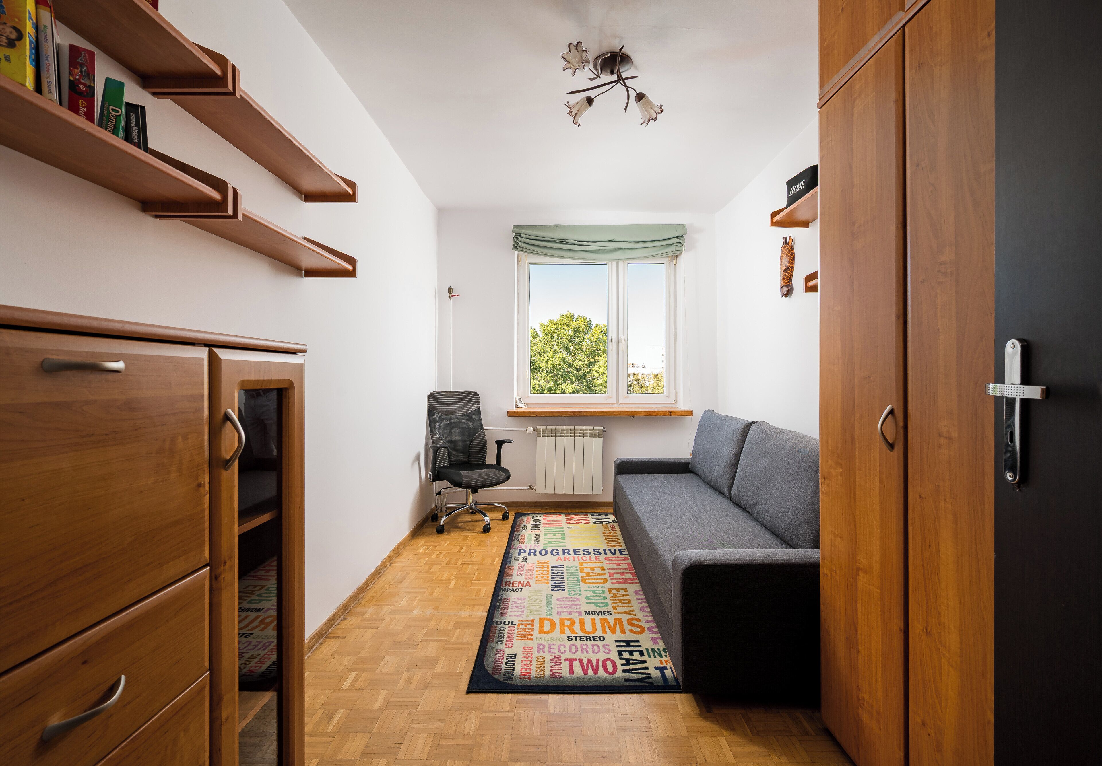 A compact room with a sofa, wooden wardrobe, and a radiator.