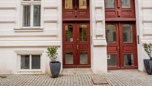 A building facade with a central double door, two windows on either side, and two potted plants.