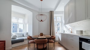 A modern kitchen with a round dining table, wooden flooring, and a built-in bench with cushions.